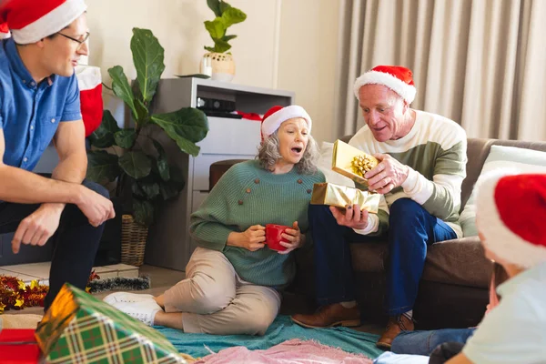 Família Caucasiana Feliz Usando Chapéus Papai Noel Desempacotando Presentes Sala — Fotografia de Stock