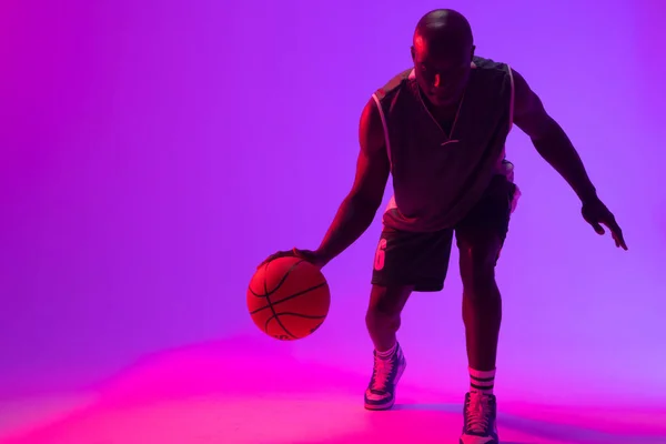 アフリカ系アメリカ人バスケットボール選手がネオンパープルの背景でバスケットボールを跳ねているイメージ スポーツ 競技の概念 — ストック写真
