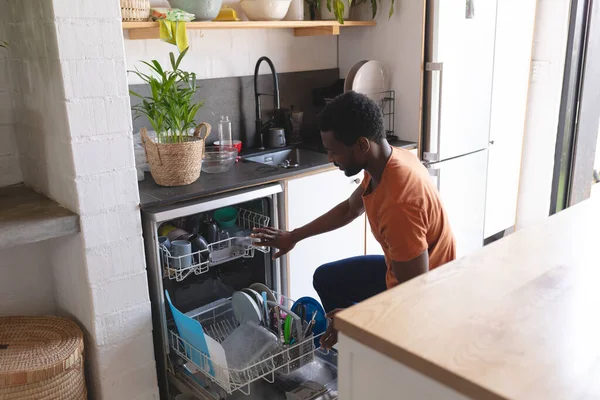 幸せなアフリカ系アメリカ人男性の掃除 キッチンで食器洗い機をアンロードします 自宅だけで質の高い時間を過ごす — ストック写真