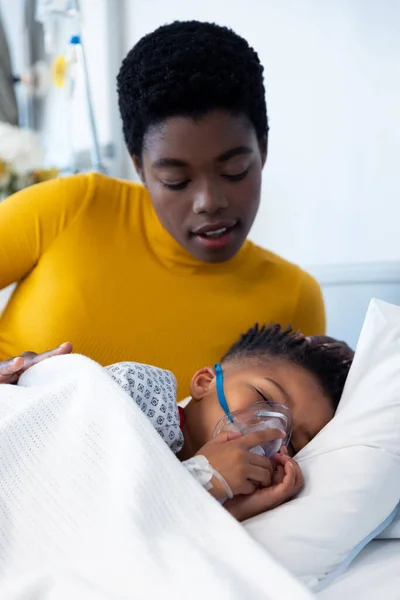 病院のベッドで人工呼吸器を装着している息子の患者の横にアフリカ系アメリカ人の母親の垂直 医療サービス — ストック写真