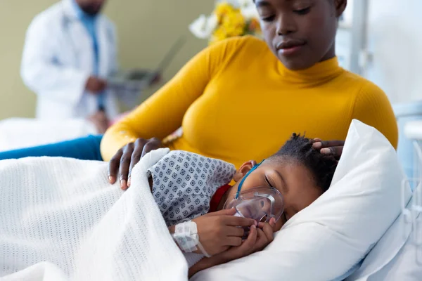 病院のベッドで眠っている人工呼吸器の息子の患者の横にアフリカ系アメリカ人の母親 医療サービス — ストック写真