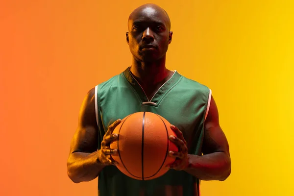 ネオンオレンジの背景にバスケットボールとアフリカ系アメリカ人バスケットボール選手の肖像画の画像 スポーツ 競技の概念 — ストック写真