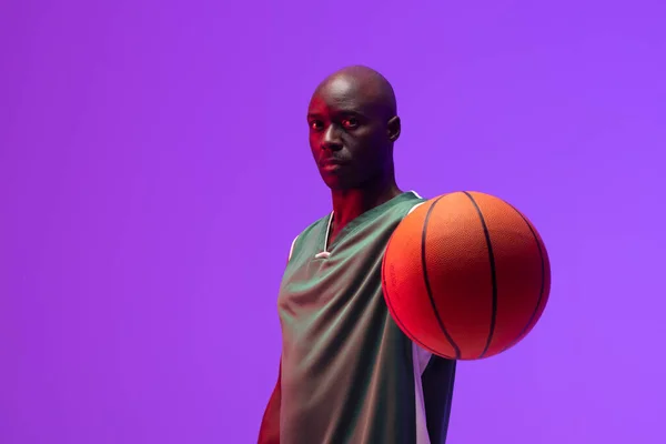 ネオン紫の背景にバスケットボールとアフリカ系アメリカ人バスケットボール選手の肖像画のイメージ スポーツ 競技の概念 — ストック写真