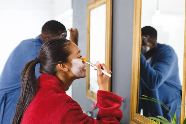 バスルームで幸せな多様なカップルは 鏡を見て クレンジングフェイスマスクを適用します 家庭生活 セルフケアと包括的な概念 — ストック写真