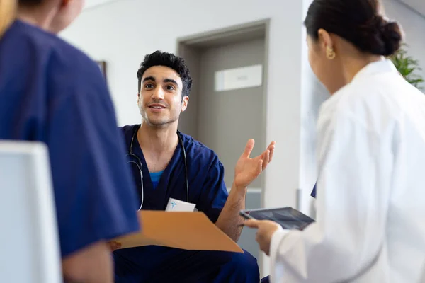 病院の多様な女性同僚と議論を交わして座っている出産の男性医師を笑顔 医療サービス — ストック写真