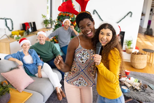 照片中快乐的两个不同的女性朋友在家里和朋友一起唱卡拉Ok庆祝圣诞节 圣诞节 庆祝活动 包容和生活方式概念 — 图库照片