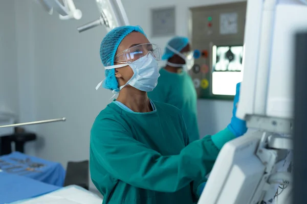 Çift Irklı Kadın Cerrah Ameliyathanede Bilgisayar Destekli Tıbbi Ekipman Kullanıyor — Stok fotoğraf