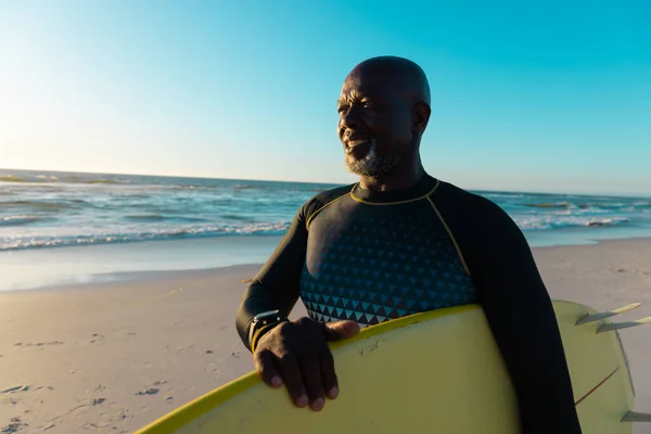秃顶的非洲裔美国老人 冲浪板站在海滩上 与大海和蓝天相映成趣 复制空间 水上运动 — 图库照片