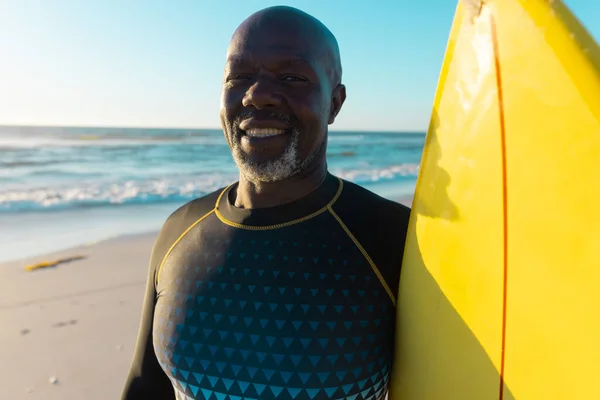 满脸笑容的秃顶的非洲裔美国老人 黄色的冲浪板站在大海和晴朗的天空中 复制空间 水上运动 — 图库照片