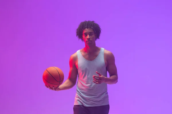 Image of biracial basketball player with basketball on neon purple background. Sports and competition concept.