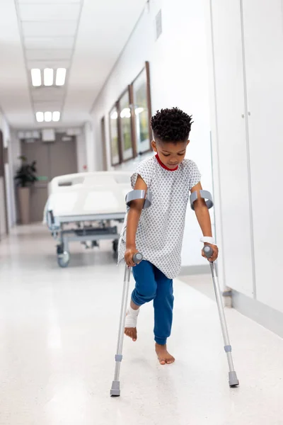 非洲裔美国男孩患者的垂直行走与拐在医院走廊与复制空间 医疗和保健服务 — 图库照片
