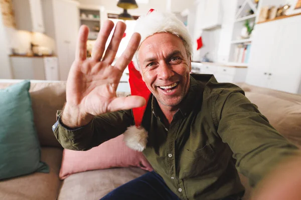 Kafkasyalı Mutlu Bir Adam Noel Baba Şapkası Takıyor Oturma Odasında — Stok fotoğraf