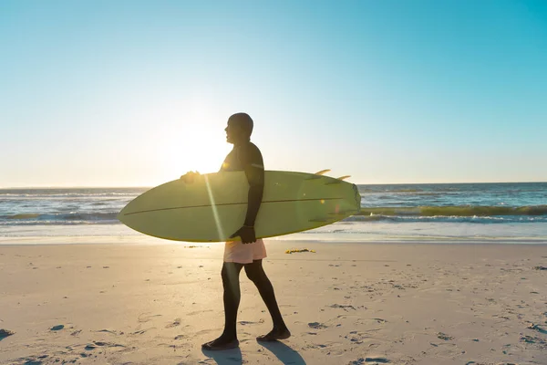 海と空に対して砂浜を歩いてサーフボードとアフリカ系アメリカ人のシニア男性の側面図 コピースペース ウォータースポーツ レクリエーション 変更なし 楽しみ — ストック写真