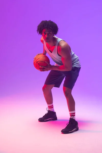 Image of biracial basketball player with basketball on neon purple background. Sports and competition concept.
