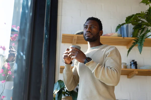 キッチンに立ってコーヒーを飲んでいるアフリカ系アメリカ人の幸せな男 自宅だけで質の高い時間を過ごす — ストック写真