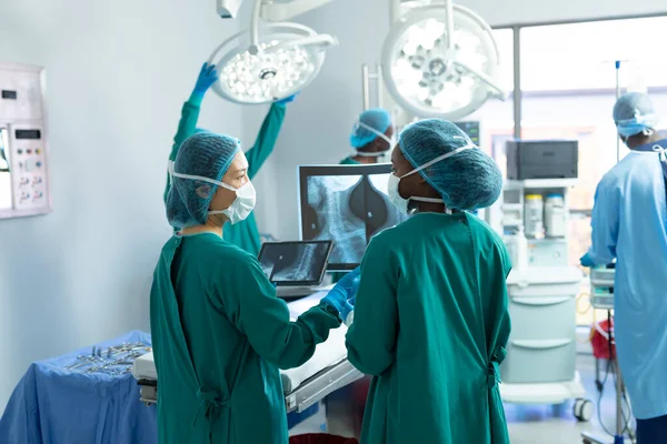 Bakifrån Två Olika Kvinnliga Kirurger Diskuterar Röntgen Operationssalen Med Kollegor — Stockfoto