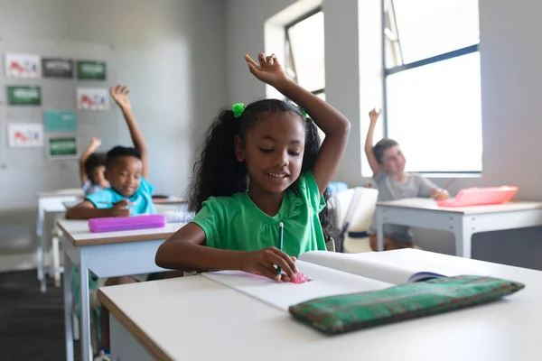 Elleri Havada Gülümseyen Çok Irklı Ilkokul Öğrencileri Sınıfta Masa Başında — Stok fotoğraf