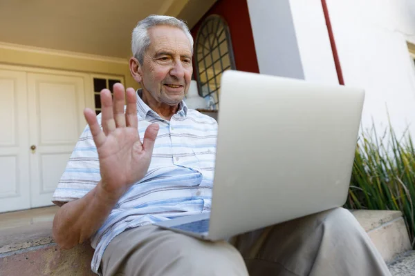 年长的高加索人呆在家里 坐在自家门前的楼梯上 使用笔记本电脑 挥挥手 检疫封闭过程中的分离分离物 — 图库照片