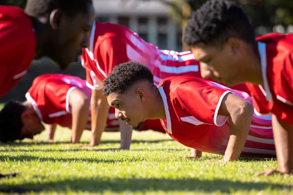 Multiracial Male Players Wearing Red Uniforms Practicing Push Ups Grassy — Stock Photo, Image