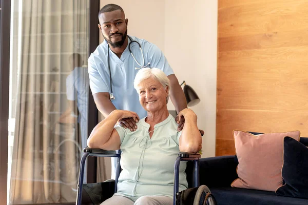 アフリカ系アメリカ人男性の健康労働者と家庭で車椅子で白人のシニア女性の肖像画 医療と定年退職シニアライフスタイルの概念 — ストック写真