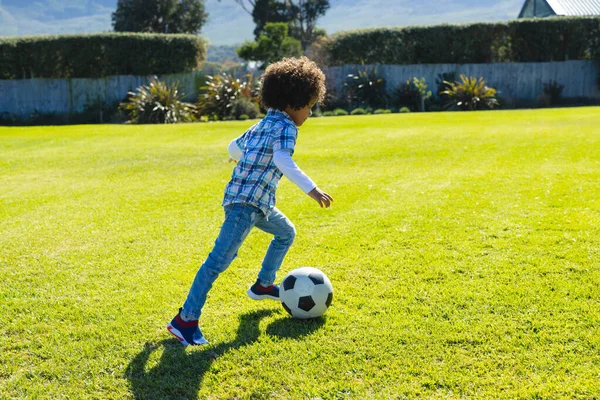 庭で芝生のフィールド上でサッカーボールを実行し キックアフロ髪を持つ出生少年の側面図 変更されていない ライフスタイル 子供時代 サッカー 楽しさとスポーツの概念 — ストック写真