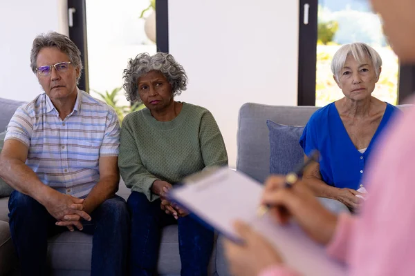 Multiracial Seniors Looking Female Therapist Writing Paper Group Therapy Session — стоковое фото