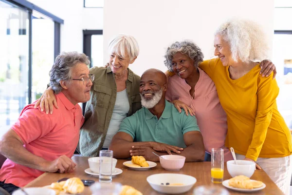 在养老院的餐桌边吃早餐时 多种族的老朋友抱着胳膊在身边享受着 愉快的 不变的 食物的 饮料的 健康的 团结的 支持的 辅助的生活和退休的 — 图库照片