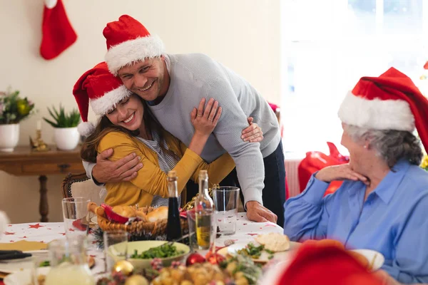 Caucasian Couple Sitting Table Dinner Together Wearing Santa Hats Embracing — Stock Photo, Image