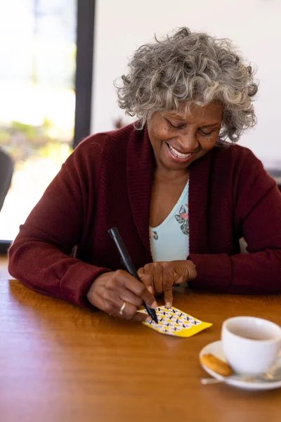 Mujer Mayor Afroamericana Sonriente Marcando Números Tarjeta Bingo Sobre Mesa — Foto de Stock