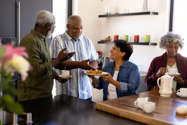 一位面带微笑的老年妇女在养老院为多种族朋友提供饼干 不变食品 辅助生活和退休 — 图库照片