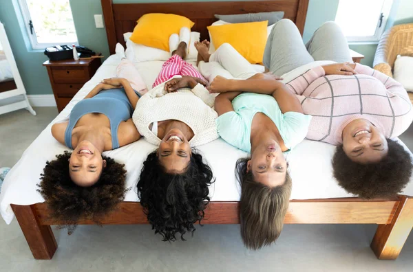 stock image High angle view of biracial cheerful young female friends lying side by side on bed at home. Unaltered, friendship, togetherness, lifestyle, resting and home concept.