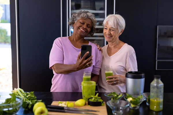Smiling Multiracial Senior Female Friends Looking Smartphone While Standing Kitchen — Stock Photo, Image