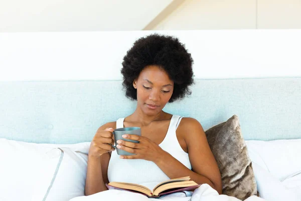 아프리카 미국인젊은 집에서 침대에서 읽으면서 커피를 마시고 있습니다 공간이죠 변경되지 — 스톡 사진