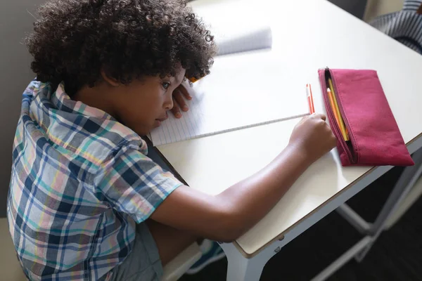 教室の机にもたれて本を持つアフリカ系アメリカ人の小学生の高角度ビュー 変化のない教育子供時代学習学校の概念 — ストック写真