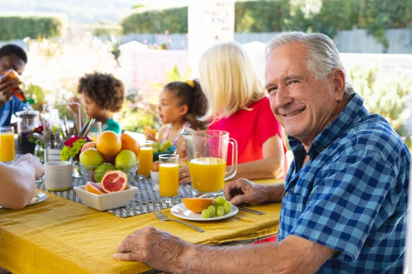 在家里餐桌边与多种族家庭共进早餐的面带微笑的老年人的画像 生活方式 饮料和退休观念 — 图库照片