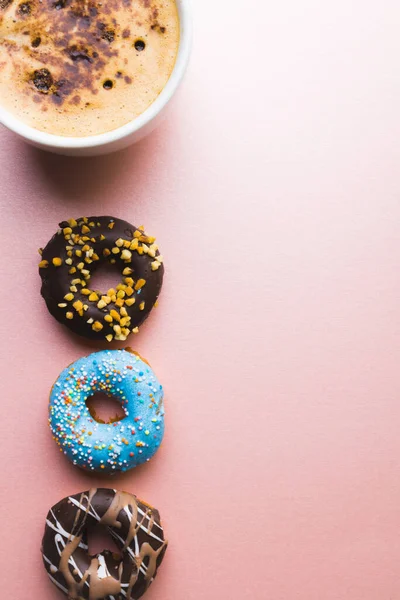 Overhead view of fresh chocolate drink in cup by donuts and copy space against colored background. unaltered, unhealthy eating and sweet food concept.