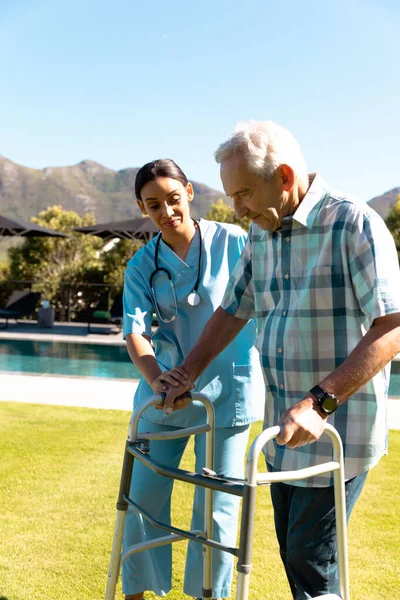 分娩时的女性保健工作者帮助高加索老年男子带着步行框架走路 医疗和退休老年人生活方式概念 — 图库照片