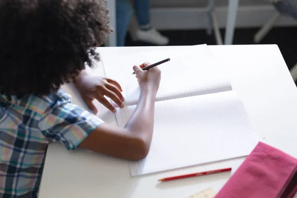アフリカ系アメリカ人の小学生が教室の机で本を書いている 無修正 子供時代 学校のコンセプト — ストック写真