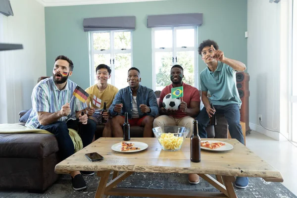 好奇的多种族男性朋友与旗帜 球观看比赛的同时享受周末在家里 不变食品 社交活动 周末活动 — 图库照片