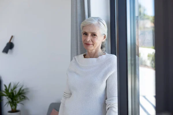 家の窓の近くに立って笑っている白人の先輩女性の肖像画 定年退職者のライフスタイルと生活コンセプト — ストック写真