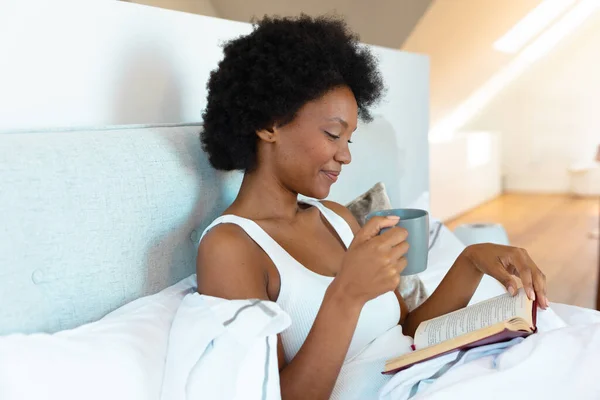 Afroamerikansk Ung Kvinna Som Håller Kaffekopp Och Läser Bok Sängen — Stockfoto