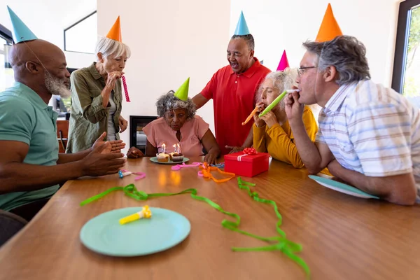 多种族的资深朋友吹响聚会号角 老年妇女吹响生日蜡烛 疗养院 派对帽 保持不变 辅助生活 — 图库照片
