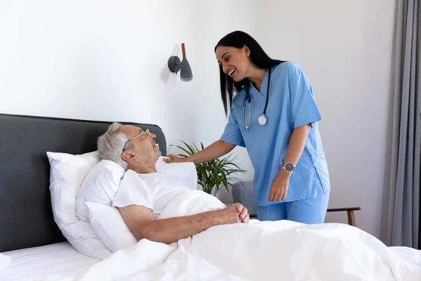 ベッドの上に寝そべっているアジア系のシニア男性と話をしている出産女性の健康労働者 医療と定年退職シニアライフスタイルの概念 — ストック写真