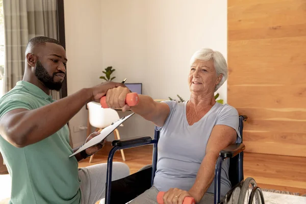 Afrykański Fizjoterapeuta Pomagający Białej Starszej Kobiecie Ćwiczyć Hantlami Koncepcja Fizjoterapii — Zdjęcie stockowe