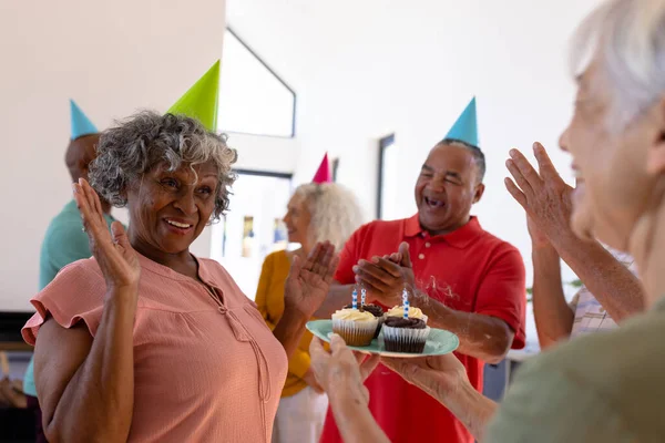 快乐的多种族老年人在庆祝生日的时候为老年妇女鼓掌唱歌 疗养院 纸杯蛋糕 保持不变 辅助生活 — 图库照片