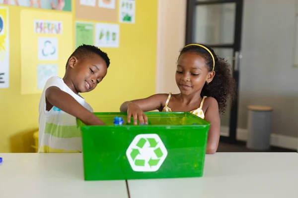 アフリカ系アメリカ人の小学生が机の上にペットボトルをリサイクル容器に入れています 変化のない教育子供時代環境浄化持続可能なライフスタイル学校のコンセプト — ストック写真