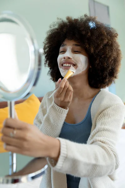 Mujer Joven Biracial Con Cabello Afro Sosteniendo Espejo Aplicando Crema —  Fotos de Stock