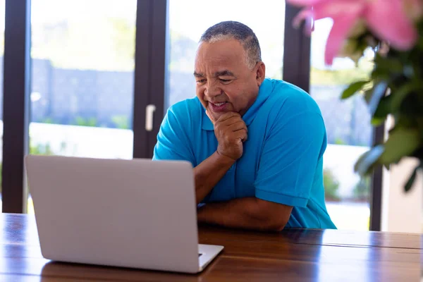 坐在桌边 手托着下巴 一边笑一边看笔记本电脑上的视频 无线技术 因特网 辅助生活和退休家庭概念 — 图库照片