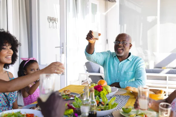 多种族快乐老人一边举杯 一边在家里与多代同堂的家人共进午餐 童年和退休的概念 — 图库照片