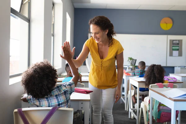 笑顔の白人の若い女性教師は 机の上に座っているアフリカ系アメリカ人の少年に5を与えます 変化のない教育子供時代教育学習学校の概念 — ストック写真